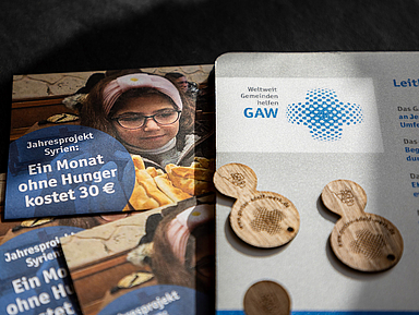 Flyer zum Jahresprojekt Syrien mit der Aufschrift „Ein Monat ohne Hunger kostet 30 €“, daneben Holzchips und ein Infoblatt mit GAW-Logo auf dunkler Oberfläche. Das Bild zeigt einen Flyer des Gustav-Adolf-Werks zum Jahresprojekt Syrien mit dem Hinweis «Ein Monat ohne Hunger kostet 30 €». Daneben liegen Holzchips und ein weiteres Informationsblatt mit dem Logo des GAW.