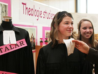 Das Foto zeigt zwei junge Frauen, die einen Talar anprobieren. 