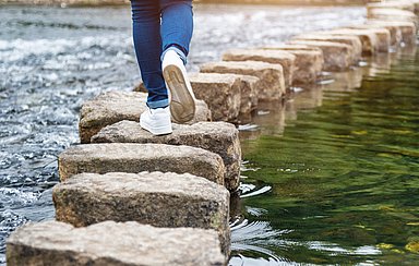 Frau überquert einen Fluss auf Trittsteinen