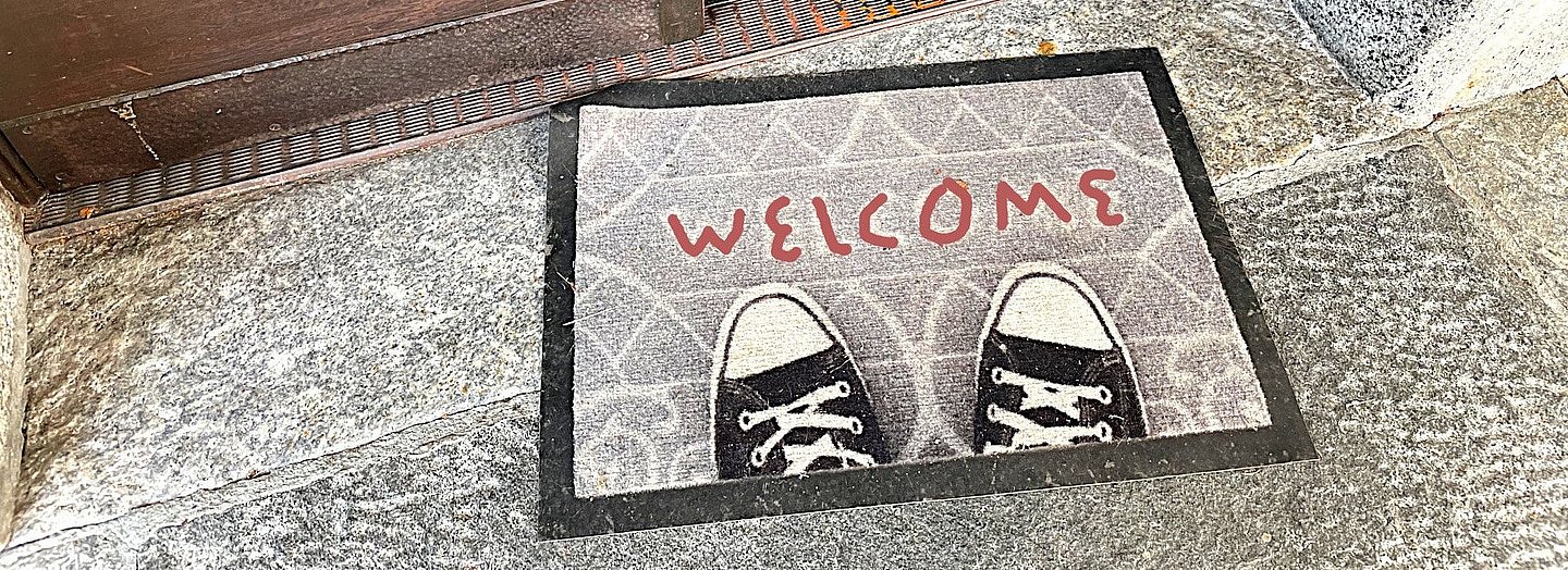 Fußmatte mit Turnschuh-Bild und "Welcome"-Aufschrift vor Kirchentür