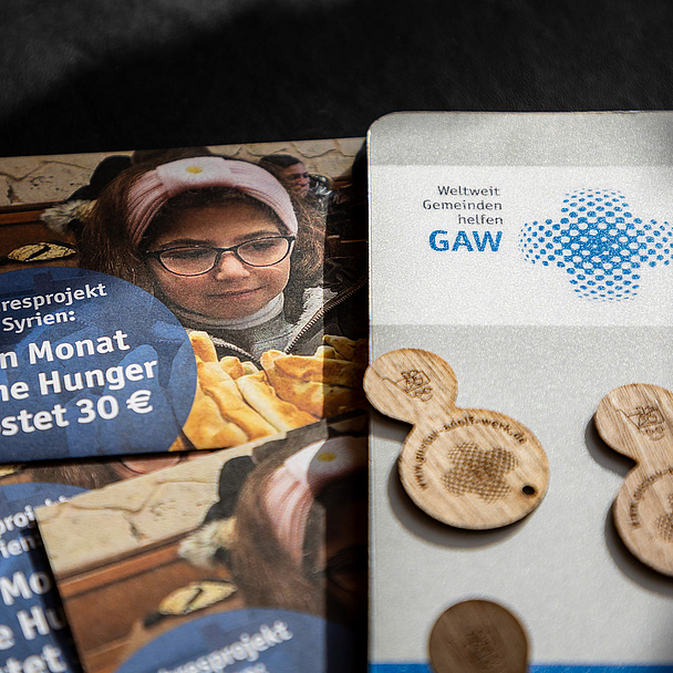 Flyer zum Jahresprojekt Syrien mit der Aufschrift „Ein Monat ohne Hunger kostet 30 €“, daneben Holzchips und ein Infoblatt mit GAW-Logo auf dunkler Oberfläche. Das Bild zeigt einen Flyer des Gustav-Adolf-Werks zum Jahresprojekt Syrien mit dem Hinweis «Ein Monat ohne Hunger kostet 30 €». Daneben liegen Holzchips und ein weiteres Informationsblatt mit dem Logo des GAW.